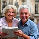 An older couple smiling while holding a map in a historic European city square.